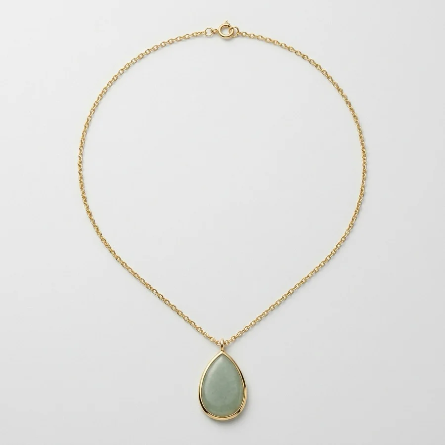 A product photograph of a gold chain necklace with a pale green teardrop stone in a thin gold bezel, laid flat on a plain light grey background