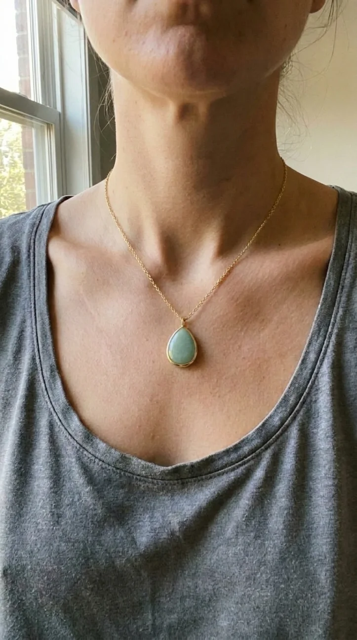 AI generated worn shot: the green stone pendant hanging at a woman's neckline over a grey vest top, in daylight